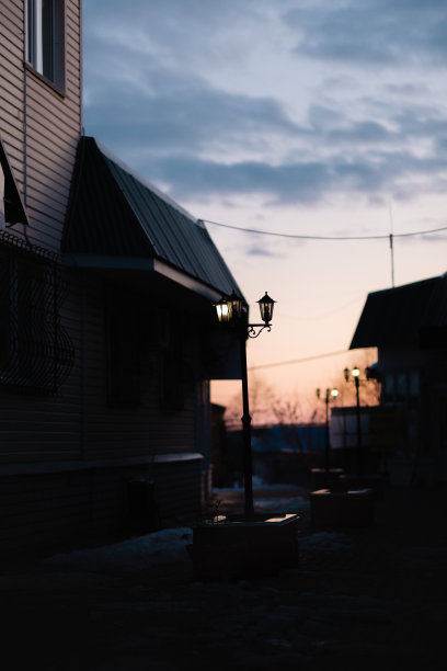 日落时分的黑暗街道。在桔黄色多云的天空下，可以看到灯光昏暗的路灯和长椅图片下载