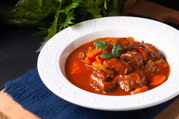 食物概念自制法国炖牛肉马伦戈在白色陶瓷汤盘木板上黑色石板背景与复制空间图片下载