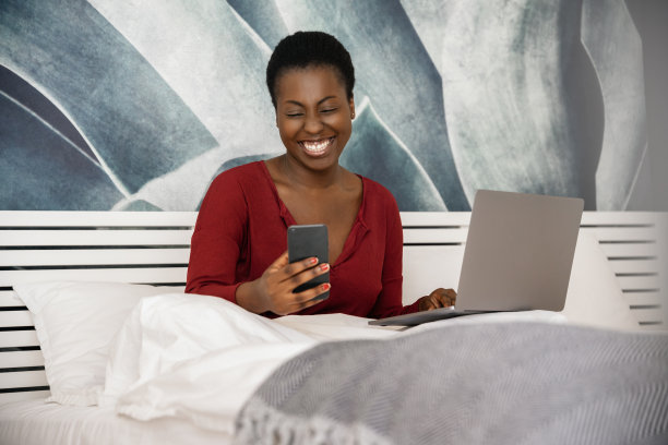 黑人非洲妇女在家工作。微笑着在床上看手机图片下载