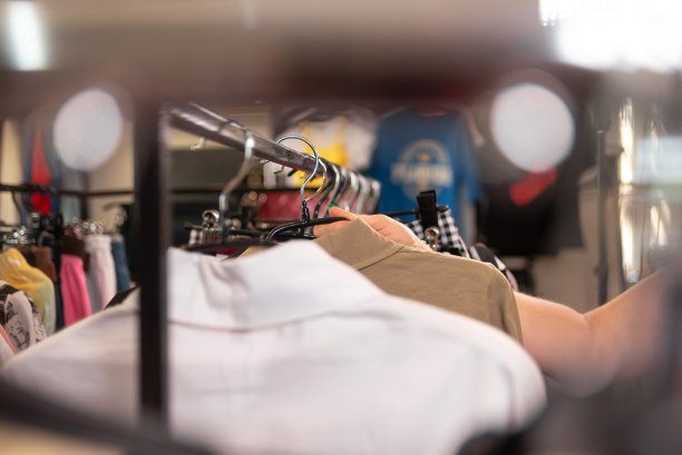 在服装厂或服装店，女人的手在挑选挂在衣架上的衣服。背景图片下载