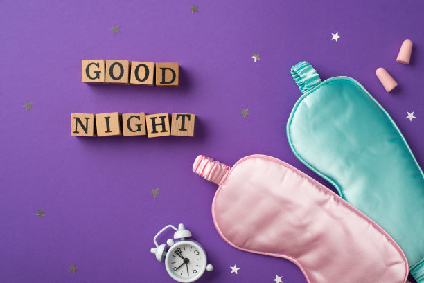 俯视图照片的一个白色警报和两个丝绸眼罩粉红色和浅蓝色的一个分散的五彩纸屑形状的星星木制立方体的字母和两个耳塞在紫色的背景图片下载