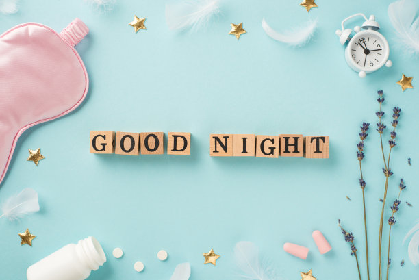 俯视图照片木制立方体晚安文本薰衣草白色闹钟粉红色丝绸睡眠面具耳塞开瓶与药丸羽毛和金色星星在孤立的淡蓝色背景图片下载