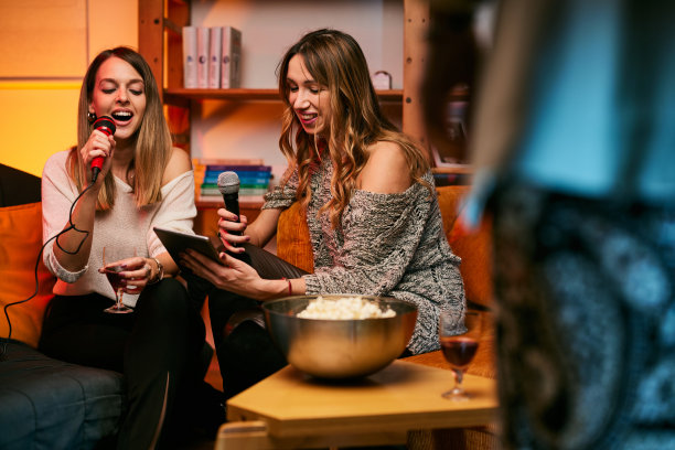 女孩们坐在家里，喝酒，在卡拉ok之夜唱二重唱。图片下载