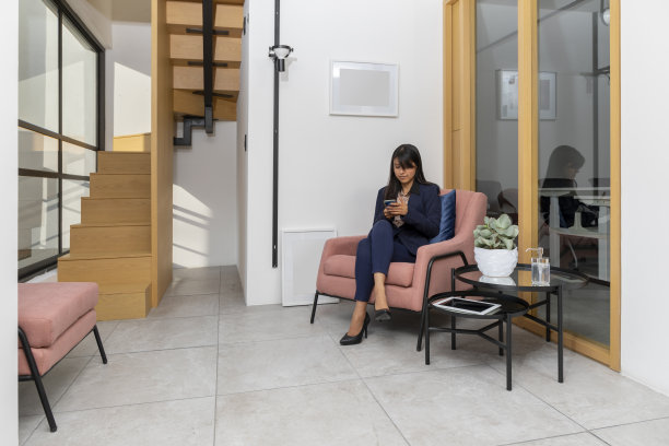 一位年轻的女高管坐在公司大厅里，一边等着，一边用手机发短信图片下载