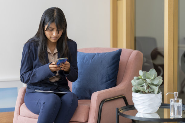 一位女士坐在扶手椅上，手里拿着手机发短信图片下载