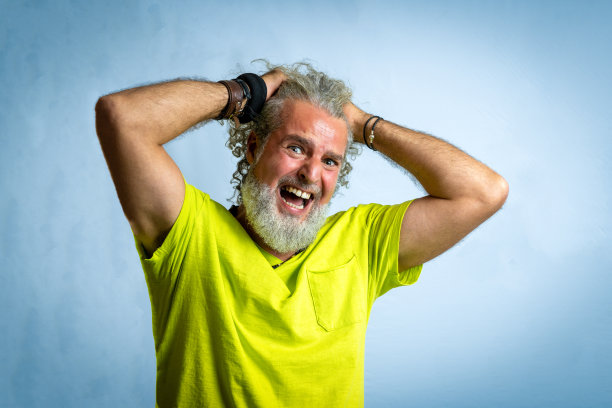 时髦的大胡子男人带着忧虑和痛苦的表情看着镜头，成年男性绝望地把手放在头发上，工作室用黄色衬衫和垃圾蓝色背景复制空间拍摄图片下载