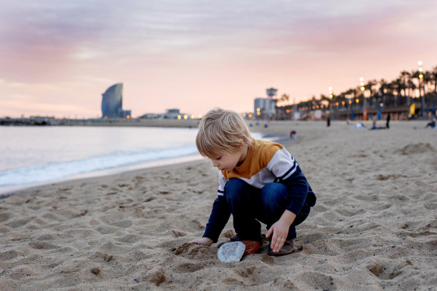 可爱的小男孩，蹒跚学步的男孩，在巴塞罗那的海滩上玩耍，一家人带着孩子旅行图片下载