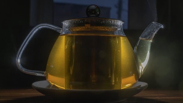 黑色背景的茶玻璃茶壶。木桌上有绿茶和茶壶。广告构成。图片下载