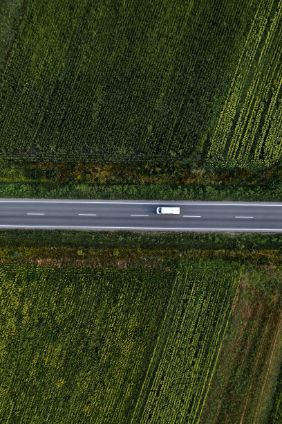 空中俯瞰白色厢式货车穿过绿色农田的道路，无人机摄影图片下载