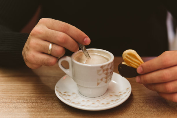 前景是一个不认识的年轻人拿着一杯咖啡和一块饼干的手。图片下载