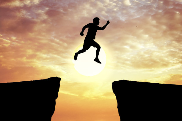 夕阳下，一个年轻人正从两座岩石山脉之间的悬崖上跳下来。图片下载