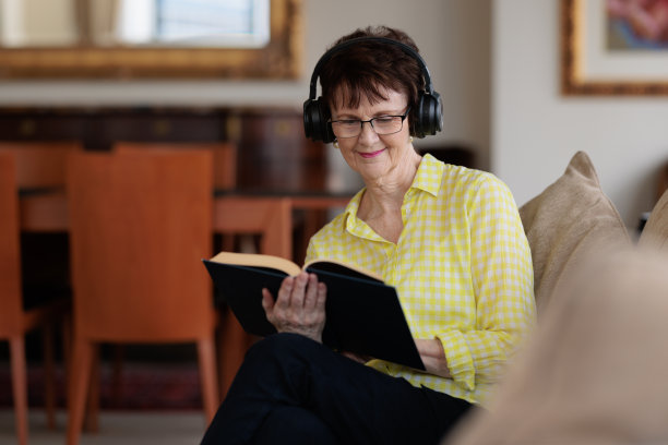 女人一边读书一边戴着耳机听音乐。图片下载