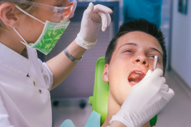 一名男孩在牙科诊所向一名女牙医展示他的牙痛的特写图像。图片下载