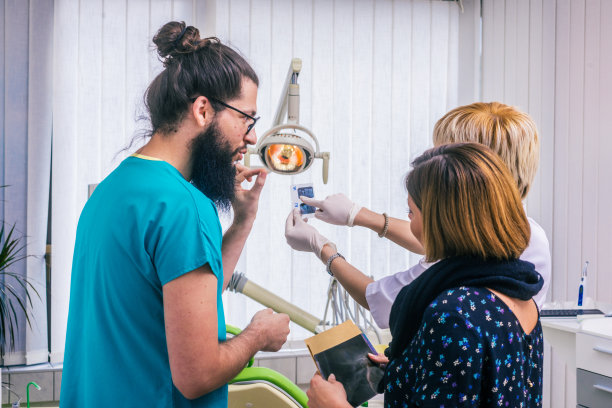 留着胡子的牙医戴着眼镜看着牙科x光扫描，和他的女病人交谈。图片下载