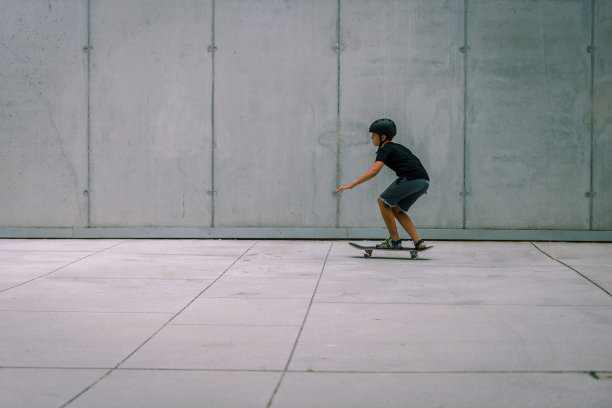 戴着头盔的黑发少女在混凝土建筑前的站台上玩滑板图片下载