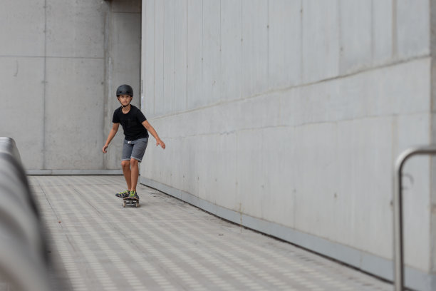 戴着头盔的黑发少女在混凝土建筑前的站台上玩滑板图片下载