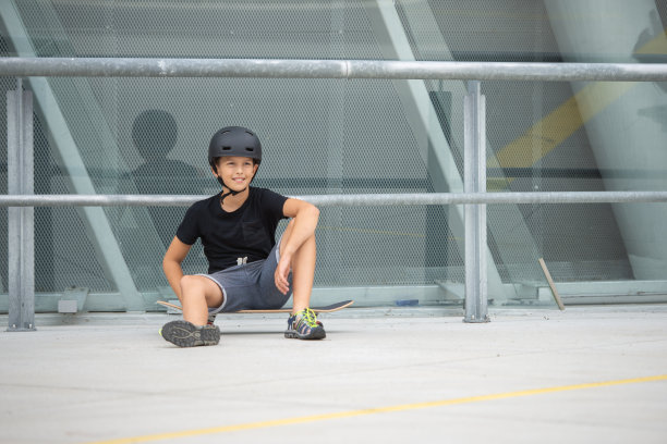 戴着头盔的黑发少女在混凝土建筑前的站台上玩滑板图片下载