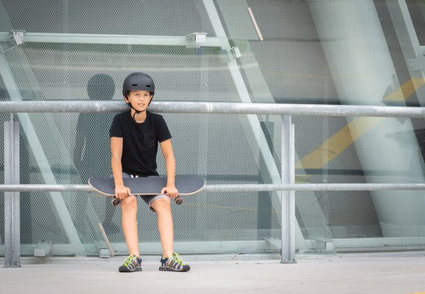 戴着头盔的黑发少女在混凝土建筑前的站台上玩滑板图片下载