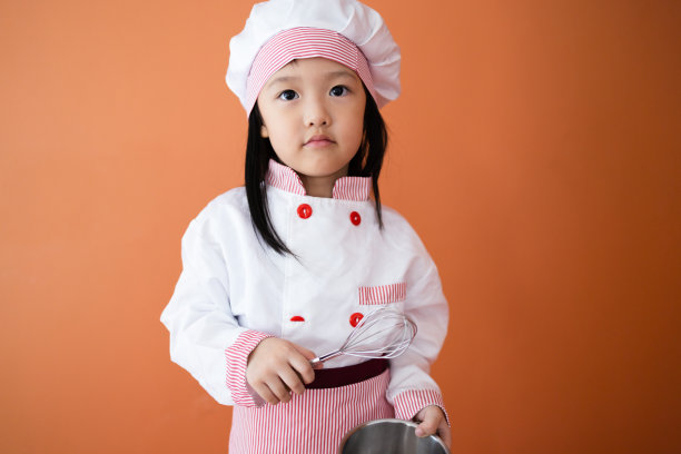 穿着厨师服的可爱亚洲女孩。为孩子学习烹饪的概念。图片下载
