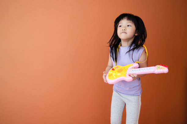 可爱的亚洲女孩与吉他玩具在橙色背景。职业和儿童活动的概念。图片下载