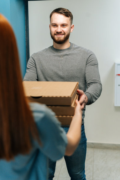 垂直拍摄的胡子男快递员在家里门口给不认识的女顾客送热披萨。图片下载