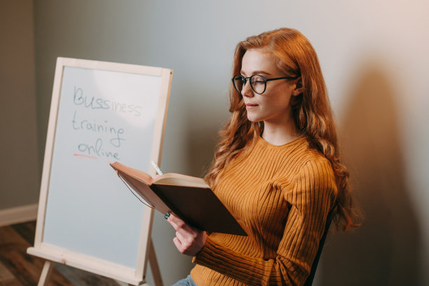 一张老师拿着课本坐在白板旁边的照片。商业的女人。图片下载