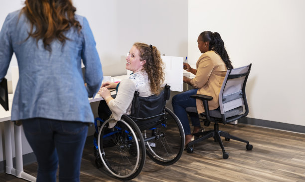 坐在轮椅上工作的女士和同事打招呼图片下载