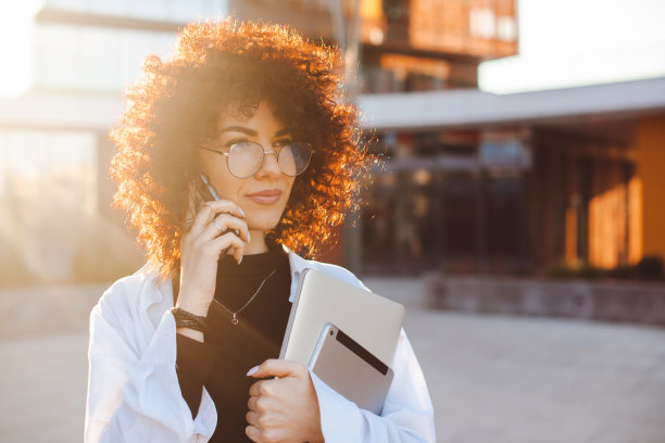 一个卷发女人的特写肖像，拿着笔记本电脑和平板电脑打电话。移动通信。卷曲的头发。图片下载