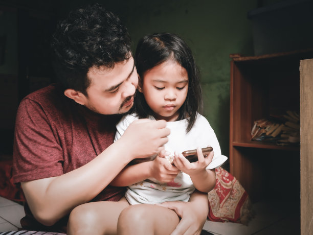 印度尼西亚雅加达，普拉加东- 2019年4月12日:一位父亲陪女儿玩智能手机图片下载