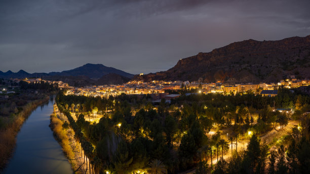 夜景照片的一个照亮的城镇周围的山旁边的河流。图片下载