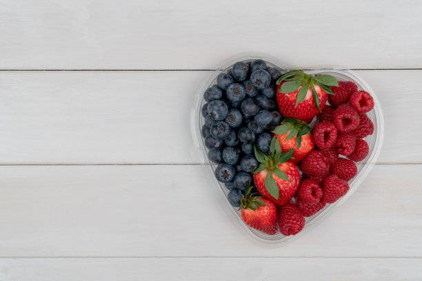 健康的混合水果，草莓，覆盆子，蓝莓在一个心形的碗上白色的桌子，俯视图，复制空间图片下载