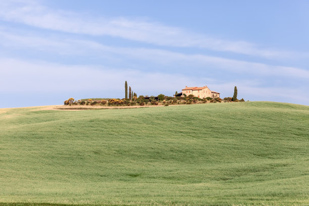 这是一座古老的农舍，夏天的时候，柏树和种植园被精心栽培的托斯卡纳山丘环绕着图片下载