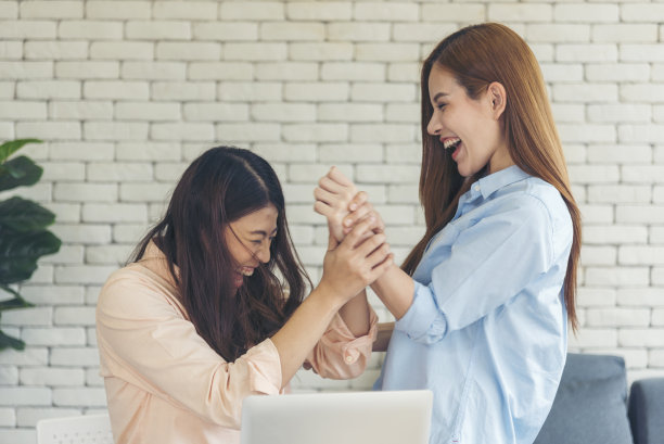 亚洲同事友谊在工作中面带微笑。幸福的两个女同事一起工作，在办公室的办公桌上开会。与笔记本电脑创业公司合作的团队合作伙伴图片下载