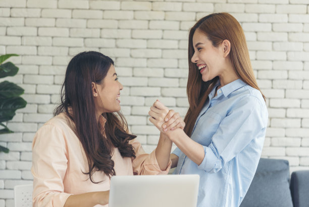 亚洲同事友谊在工作中面带微笑。幸福的两个女同事一起工作，在办公室的办公桌上开会。与笔记本电脑创业公司合作的团队合作伙伴图片下载