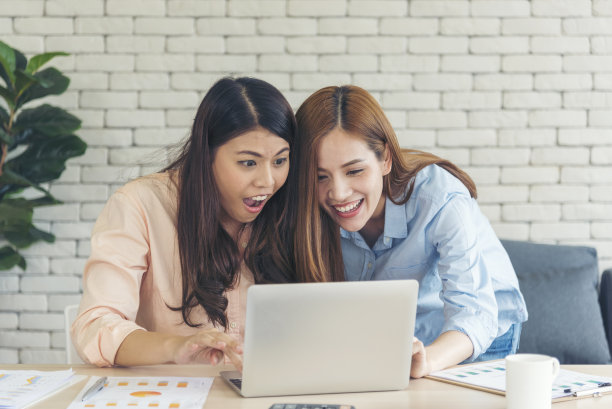 亚洲同事友谊在工作中面带微笑。幸福的两个女同事一起工作，在办公室的办公桌上开会。与笔记本电脑创业公司合作的团队合作伙伴图片下载