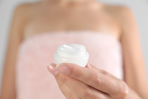 年轻女子拿着一罐奶油在灰色背景上，特写镜头图片下载