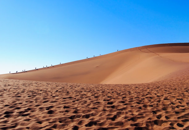 在纳米比亚的纳米布沙漠，低角的沙丘和远处攀登的人们图片下载