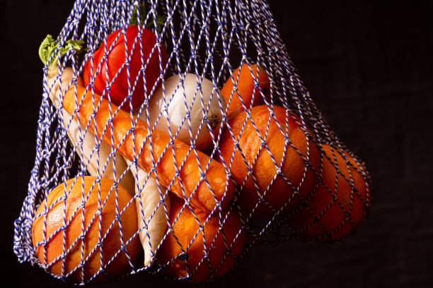 照片串袋与新鲜的水果和蔬菜-可重复使用的环保购物袋与植物食品-生素食柑橘和洋葱番茄胡萝卜和日本萝卜在黑暗的背景图片下载