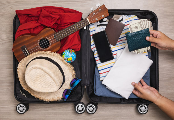 俯视图关闭男性手组织行李。把衣服和裤子放在手推车里，准备出国。为暑假旅行准备行李。旅行者配件，打开行李。图片下载