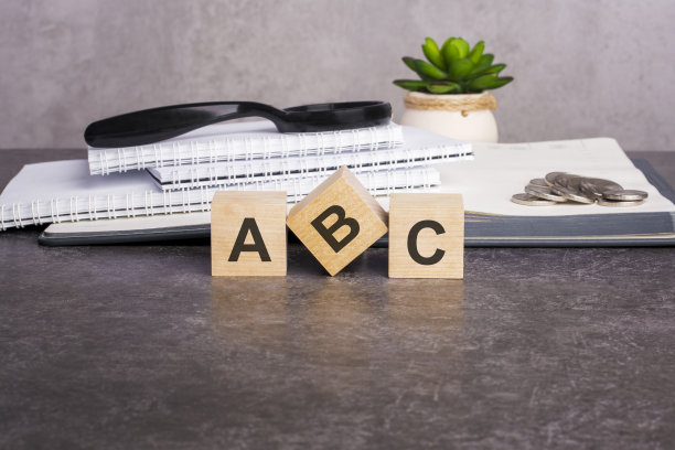 字母ABC写在灰色背景的木制立方体上。木质元素的特写。背景是一个绿色的花在浴缸里。图片下载