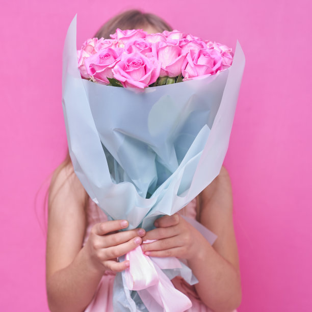 一个穿着粉红色连衣裙，手捧玫瑰花束的女孩，躲在鲜花后面图片下载