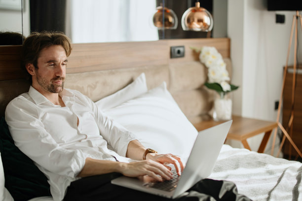 商人躺在酒店的床上用笔记本电脑图片下载