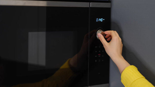 在家里，妇女用现代微波炉加热一盒食物作为零食午餐图片下载