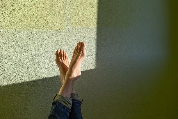 腿了。穿着牛仔裤，光着脚站在绿色的墙上。自然侧光照明图片下载