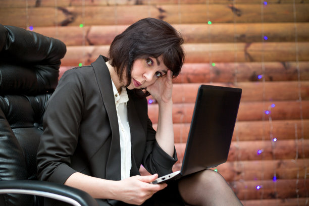 一个疲惫的黑发女人正坐在椅子上，手提电脑托着她的头图片下载