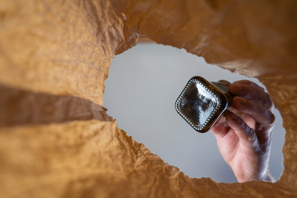 一只手把一只黑色的瓶子扔进一个纸袋。一个成熟男人的手把玻璃瓶放在打开的棕色袋子上。从下往上射击。关闭了。有选择性的重点图片下载