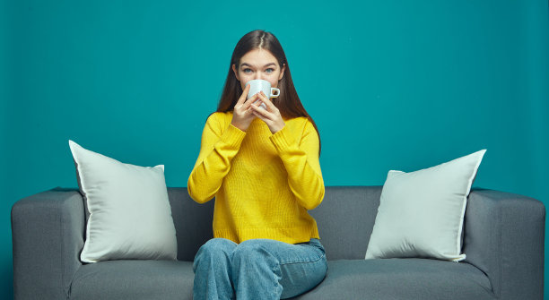 快乐的现代年轻女孩喝热茶或咖啡，从杯子坐在沙发上看系列或有趣的电影图片下载