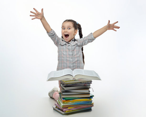 迷人的小女孩惊奇地坐在一大堆书前图片下载