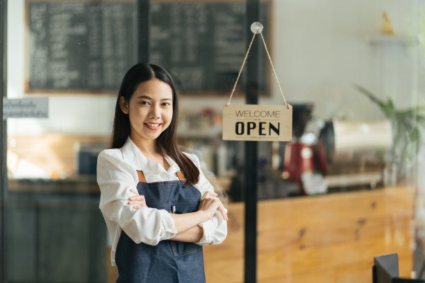 亚洲快乐女商人是一个穿着围裙的服务员，咖啡馆的老板站在门口，写着“开”的牌子等待顾客。小型经营理念，咖啡馆和餐厅图片下载