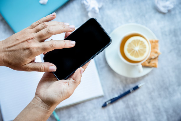 在家庭办公室平板电脑上拿着黑屏的手机，拿着笔记本电脑，喝着茶，做着自由工作。网上购物或送货图片下载